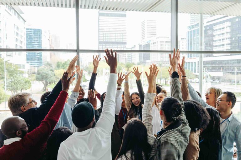 Group of businesspeople celebrating teamwork with hands raised together in a modern office. Happy colleagues showing unity and success.